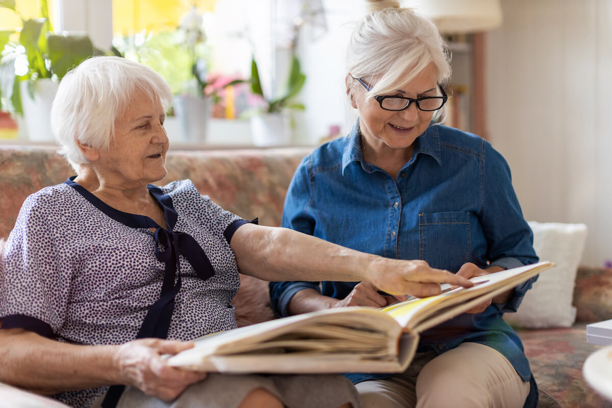 Dementia care-Senior woman and her adult daughter looking at photo album together on couch in living room