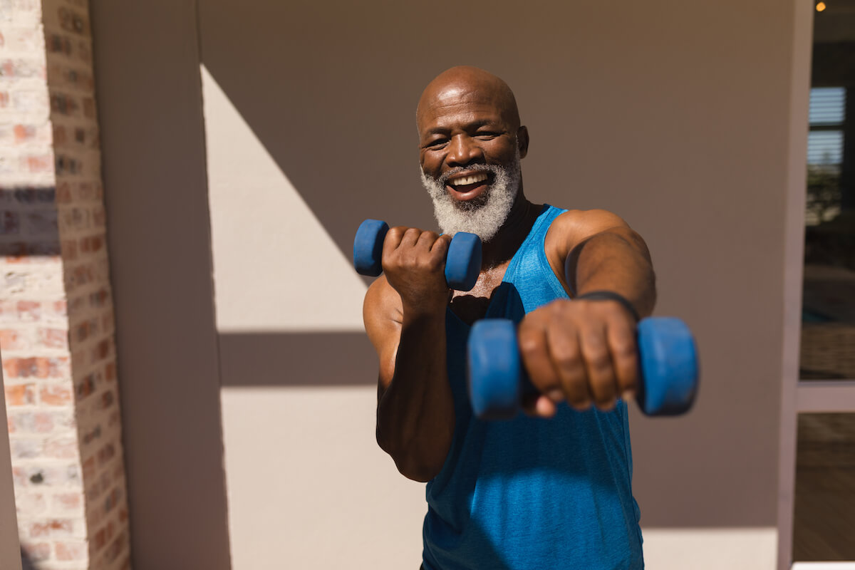 Front view of active senior African American man training arms with dumbbells in the backyard of home (1)