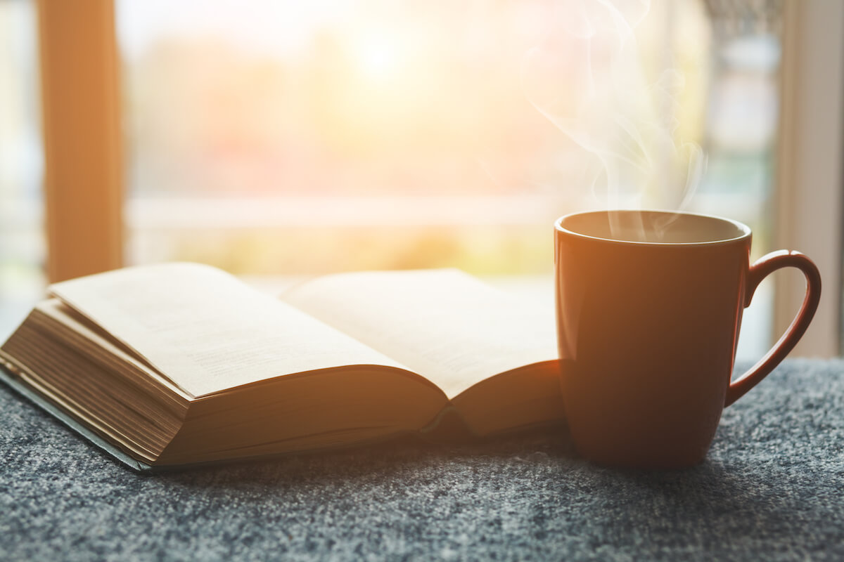 cup of fresh tea or morning coffee and open book at home at morning light, reading book and drinking coffee concept