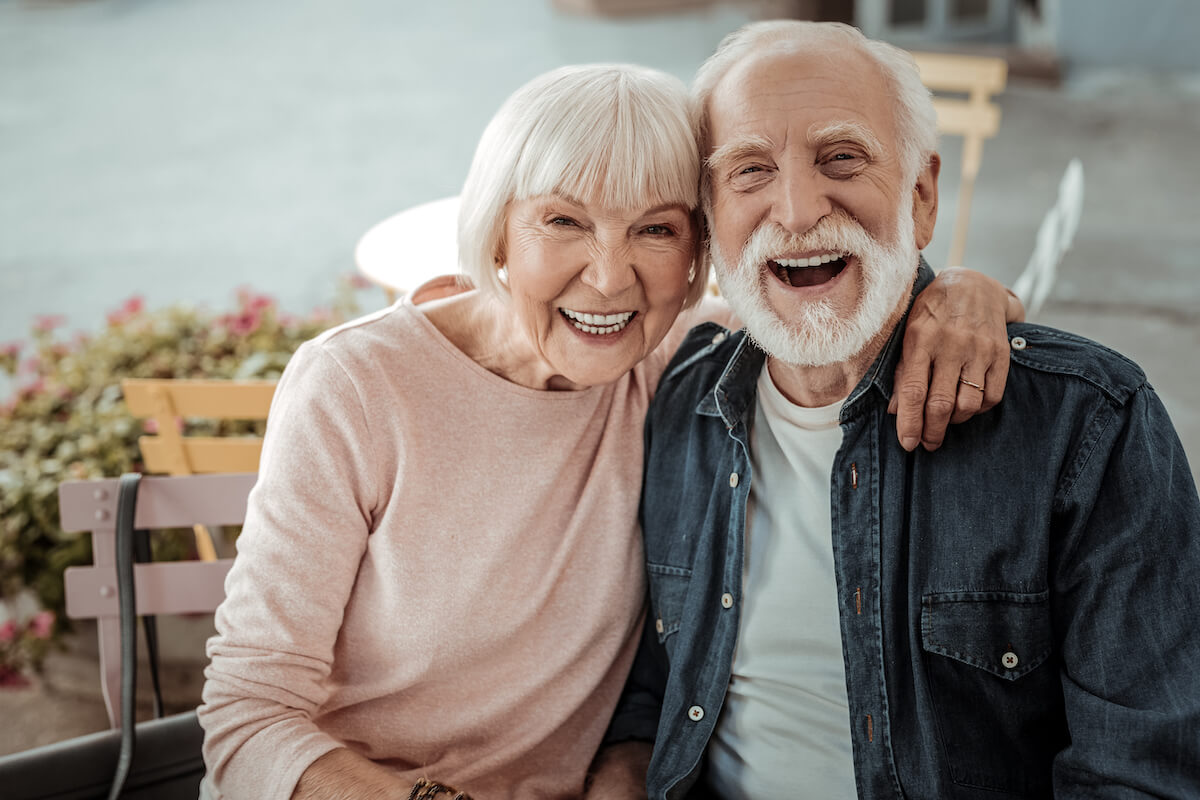 Happy aged couple. Positive aged woman sitting with her husband while hugging him
