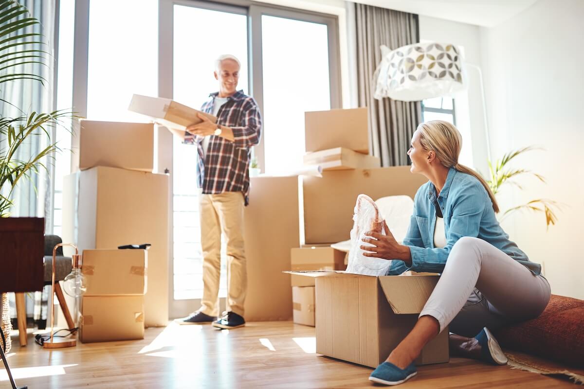 Senior Living Apartment Real estate, property and a senior couple moving house while packing boxes together in their home. Box, investment and retirement with old people unpacking in the living room of their new apartment