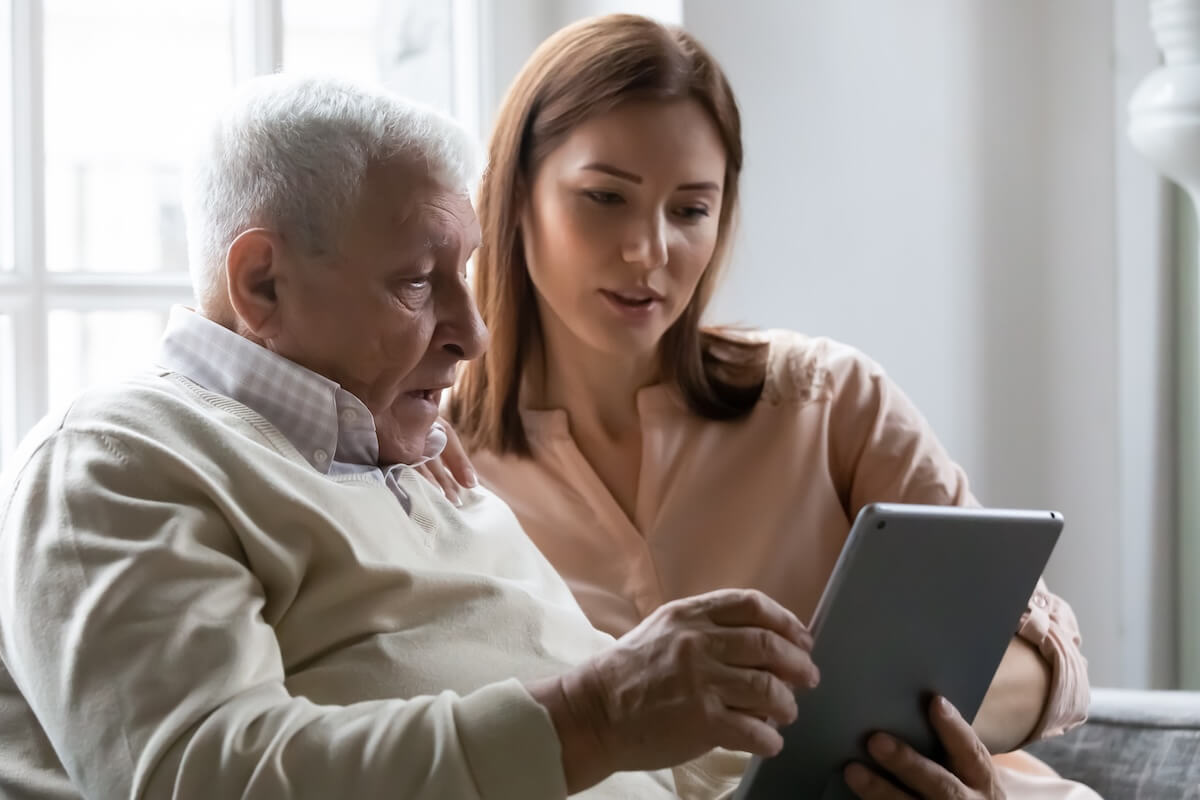 Caring grownup daughter teaching older father to use computer tablet close up, pointing at screen, mature man asking questions about mobile device to young woman, elderly and technology concept evaluating senior living options
